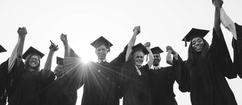 A group of graduates smiling and raising their arms.